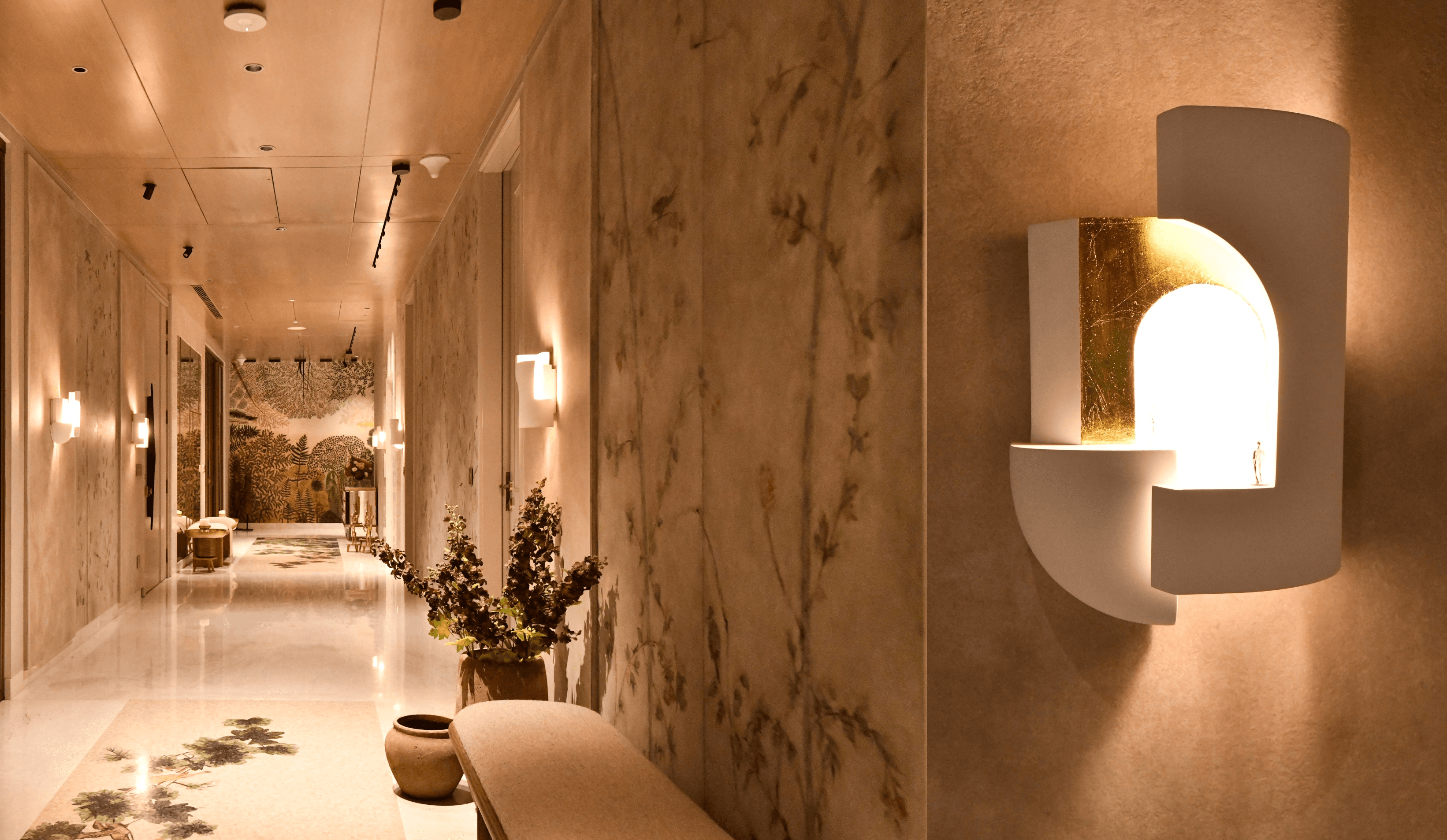 A luxurious, marble-clad corridor with warm ambient lighting and sculptural wall sconces creates an elegant, boutique-hotel-inspired ambiance.